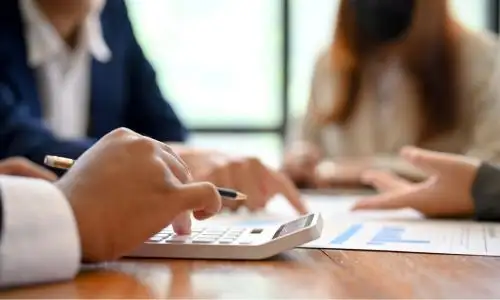 des mains pos&eacute;es &agrave; c&ocirc;t&eacute; d'une calculatrice moderne et de graphiques financiers