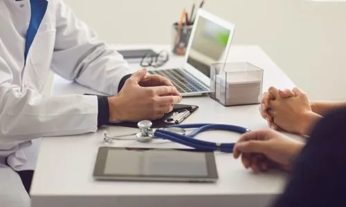 Zoom sur les mains d’un patient et son proche face à un médecin.