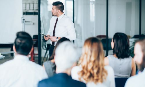 Une dizaine de personnes, dans une salle, écoutent un formateur.