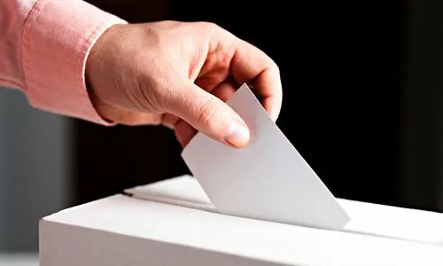 Zoom sur la main d’un homme qui met son enveloppe dans l’urne de vote.