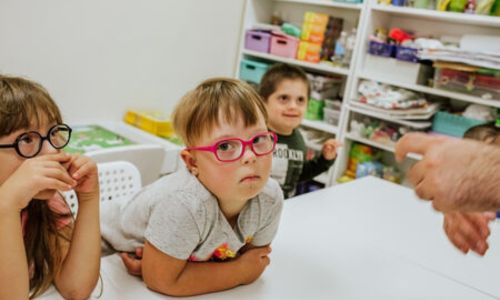 Les mains d'un enseignant s'approchent d'un enfant porteur de trisomie,en classe