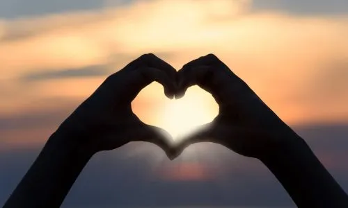 2 personnes unissent leurs mains pour former un c&oelig;ur face &agrave; un coucher de soleil