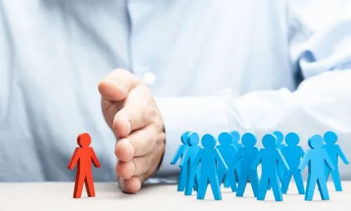 Une main sépare une figurine rouge isolée d’un groupe de figurines bleues.