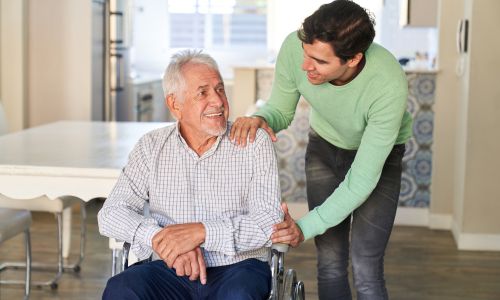 un homme âgé en fauteuil roulant et un jeune homme à l’intérieur d’une maison