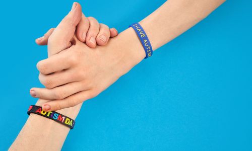 Deux mains s’empoignent avec un bracelet «autisme», sur un fond bleu