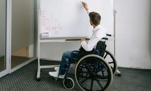 Un homme en fauteuil roulant &eacute;crit sur un tableau blanc
