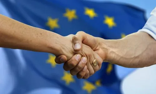2 hommes se serrent la main devant un drapeau européen.