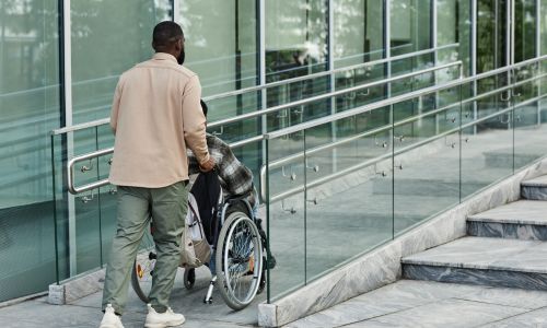 Un homme en pousse un autre en fauteuil roulant sur une rampe près d’escaliers.