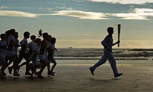 Un porteur de la flamme qui court avec un groupe de personnes sur la plage.