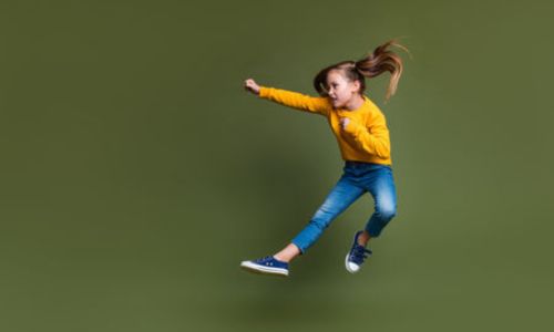Une petite fille saute en l’air, le poing levé.