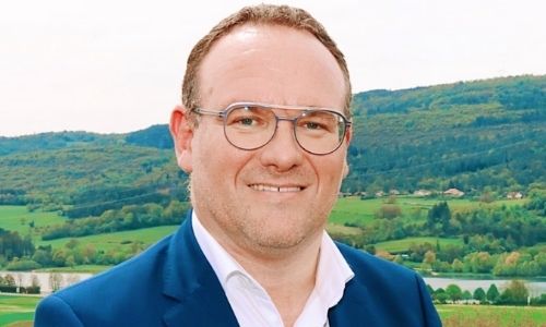 Portrait de Damien Abad, souriant, devant un paysage de campagne