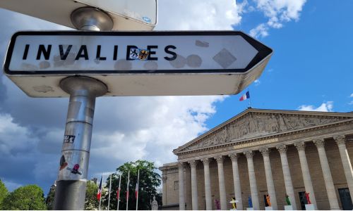 Photo de l’Assemblée nationale avec un panneau routier indiquant « invalides »