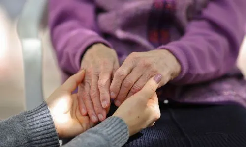 Une jeune femme tient les mains de sa maman âgée.