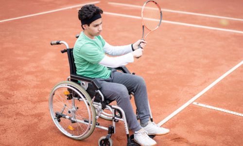 Jeune garçon en fauteuil roulant qui pratique le tennis.