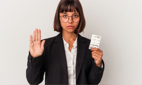 Jeune femme avec des medicaments dans une main et faisant barrage de l'autre