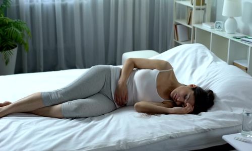 Une femme allongée sur un lit qui se tient le ventre.