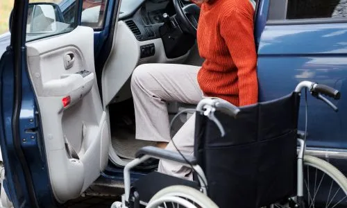 Une personne en fauteuil roulant entre dans sa voiture, côté conducteur.