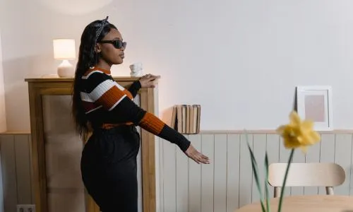 Une femme noire, aveugle, avec des lunettes de soleil, marche dans un salon.