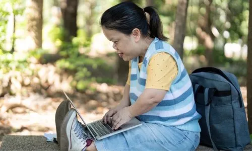 Personne avec achondroplasie utilisant un ordinateur portable dans un parc