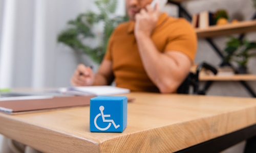 Employé à son bureau, sur lequel est posé un cube orné d'un fauteuil roulant