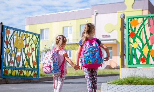 2 fillettes, se tenant la main, marchent vers une école.