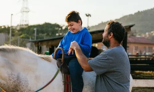 Un enfant avec une paralysie c&eacute;r&eacute;brale sur un cheval, soutenu par un homme.