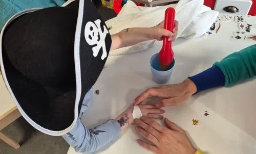 Un enfant avec un chapeau pirate essaye de mettre une cuillère dans un récipient