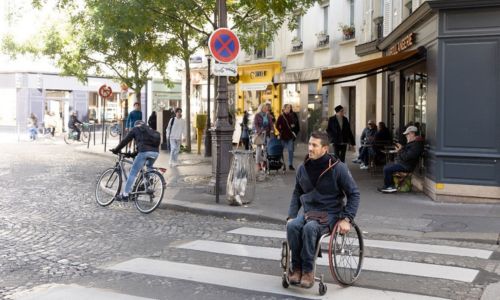 Un homme en fauteuil roulant traverse un passage piéton dans un QAA.