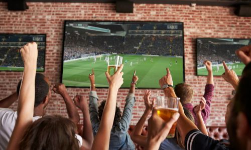 Des téléspectateurs lèvent les bras devant un match de foot diffusé dans un bar.