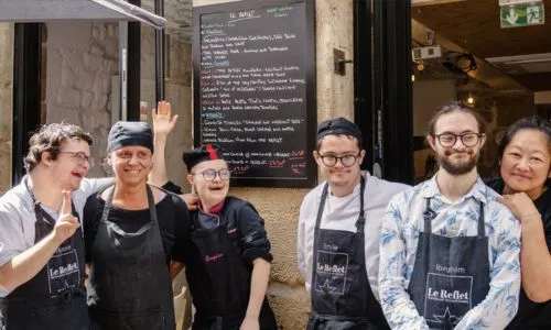 Les serveurs avec trisomie posent et sourient devant le restaurant.