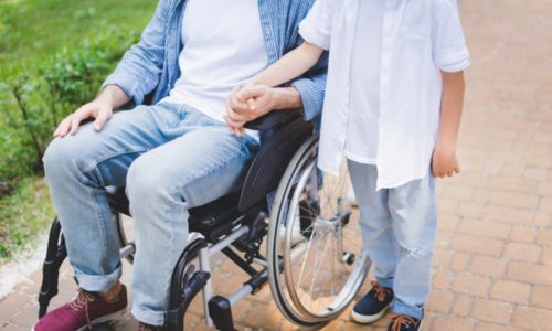 Un fils tient la main de son père en fauteuil roulant.