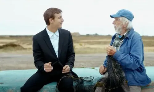 Michel et Grégoire parlent, assis sur la coque d’un bateau.