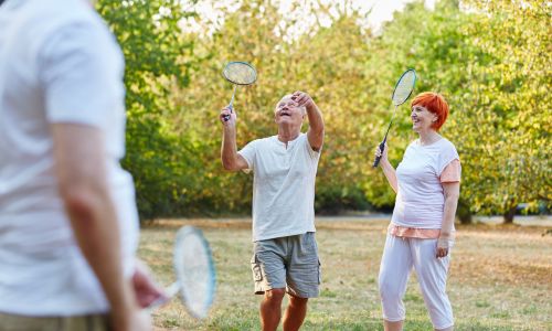 Des seniors jouent au badminton dans un jardin.