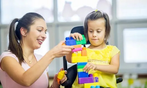 Une femme fait des Lego avec une fillette handicapée.