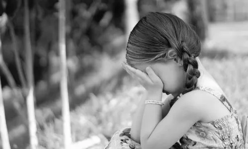 Une petite fille accroupie se tient le visage, l'air triste.