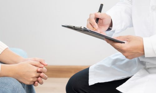 Un médecin en blouse blanche prend des notes sur un carnet face à un patient.