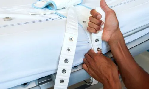 Un infirmier attache une ceinture de contention sur le lit.