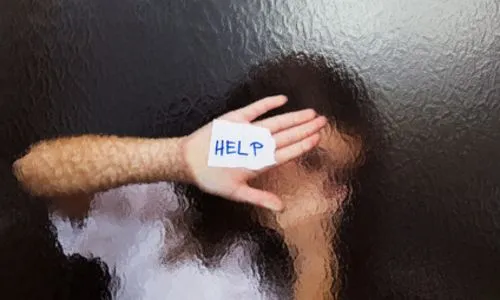 Femme derrière une vitre qui brandit un écriteau « help ».