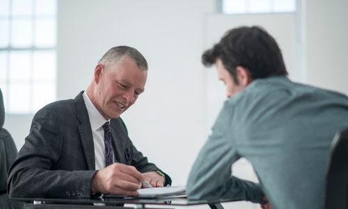 Un conseiller en costume parlant à un homme de dos assis à un bureau