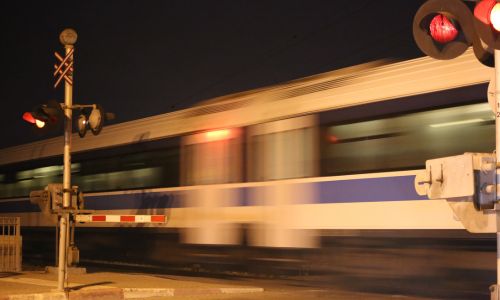 Un train de nuit sur un passage à niveau fermé, indiqué par un feu rouge.