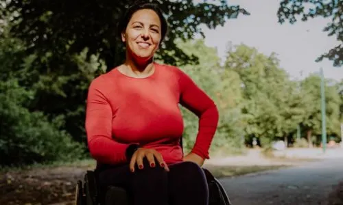 Portrait de Sandra Laoura, en fauteuil roulant, sur un chemin bois&eacute;.