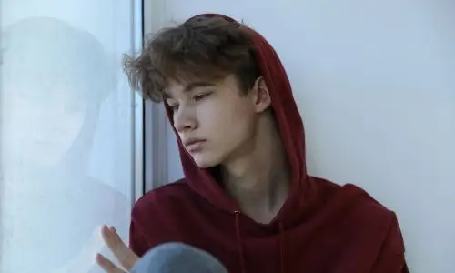 Un adolescent d&eacute;prim&eacute; s'appuie contre une fen&ecirc;tre.