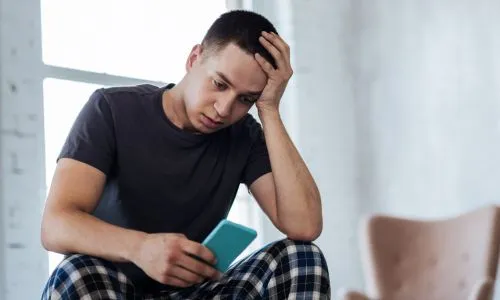 Un jeune homme triste devant son t&eacute;l&eacute;phone