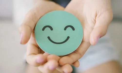 Des mains tiennent un papier vert en forme de visage qui sourit.