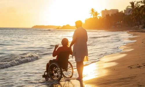 Une personne en fauteuil roulant, sur la plage, avec son proche.