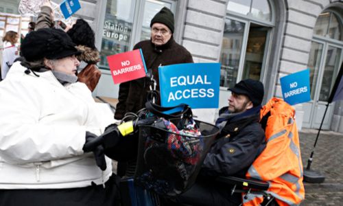 2 personnes en fauteuil tiennent des pancartes «Equal access» (accès égal).