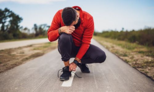 Un coureur au bord de la route, la mine baissée, pose sa tête sur son genou.