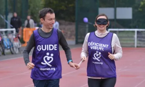 Une femme aveugle court, reliée à son guide, dans un stade.