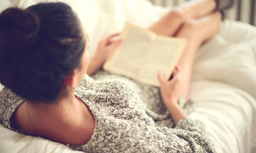 une femme lit un livre, allongée dans un canapé