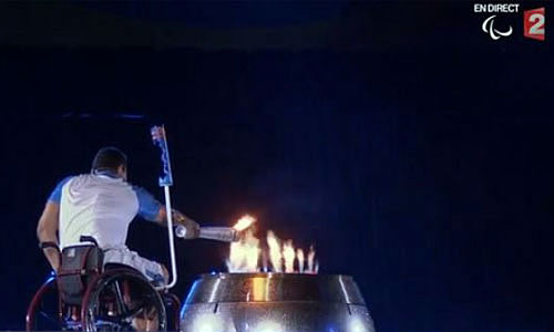 Sportif en fauteuil roulant allumant la vasque paralympique